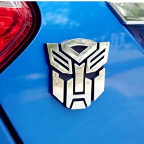 Emblème métallique Autobot sur voiture bleue, design stylisé et reflet chromé – Transformers.